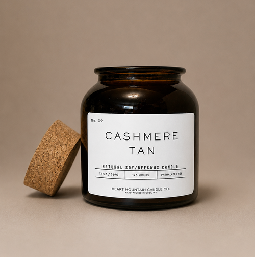 Amber glass Cashmere Tan candle with cork lid on a beige background.