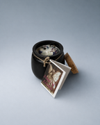 An open black cauldron-shaped candle with a cork lid beside it and a 'Wings of Wisdom' tag.