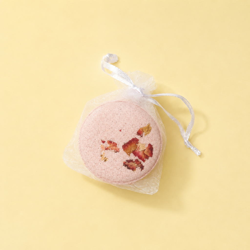 A Joy bath bomb in a mesh drawstring bag on a yellow background.