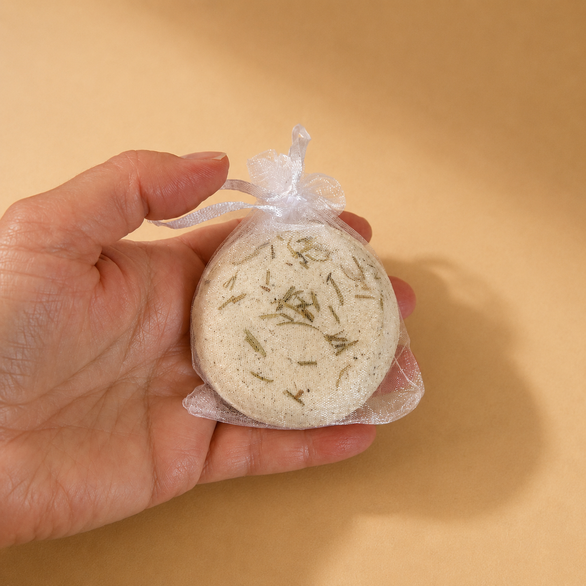 A hand holding a Ground bath bomb in a mesh drawstring bag.
