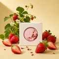 A boxed Joy bath bomb styled with fresh strawberries and small white flowers.