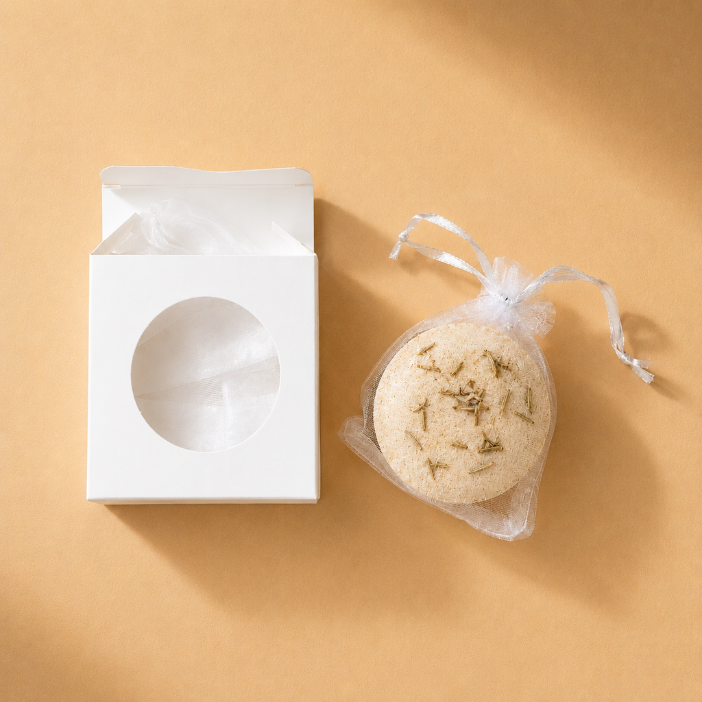 An open box beside a beige Ground bath bomb in a mesh drawstring bag.