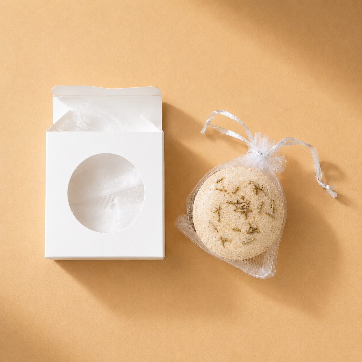 An open box beside a beige Ground bath bomb in a mesh drawstring bag.
