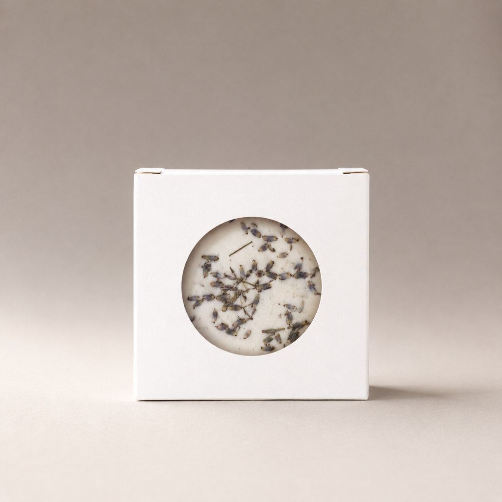 White box with a circular window showing dried botanical pieces inside, on a warm gray background.