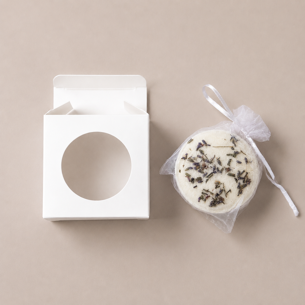Open white gift box with circular window next to a round Unwind bath bomb wrapped in mesh and ribbon.