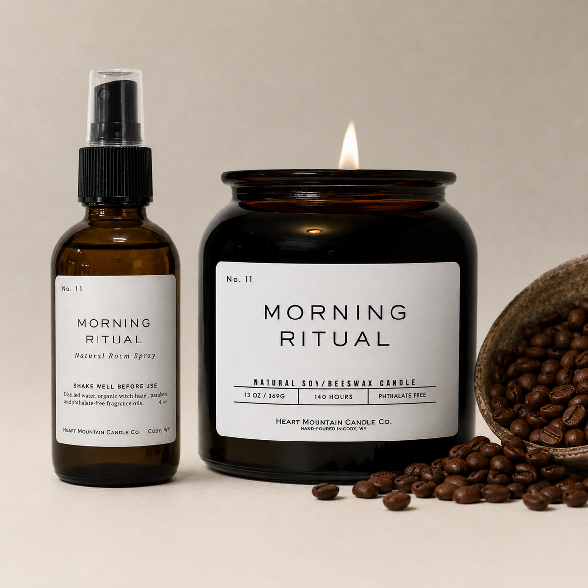 A Morning Ritual room spray bottle and lit candle jar, styled with scattered coffee beans.