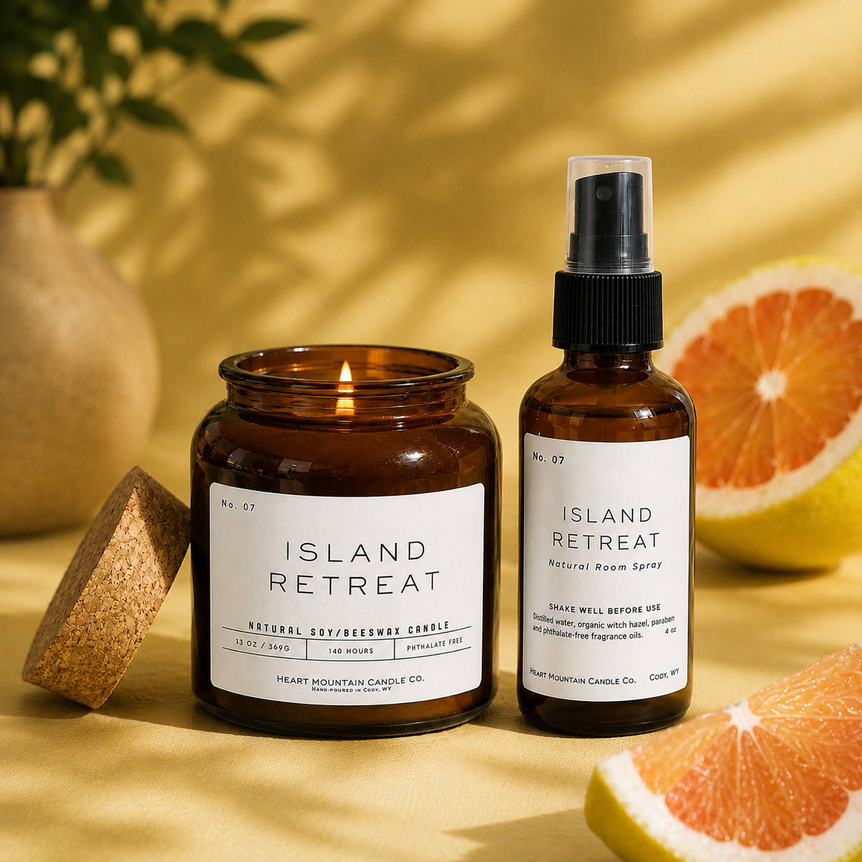 A lit Island Retreat candle jar and room spray bottle styled with citrus fruit and greenery.